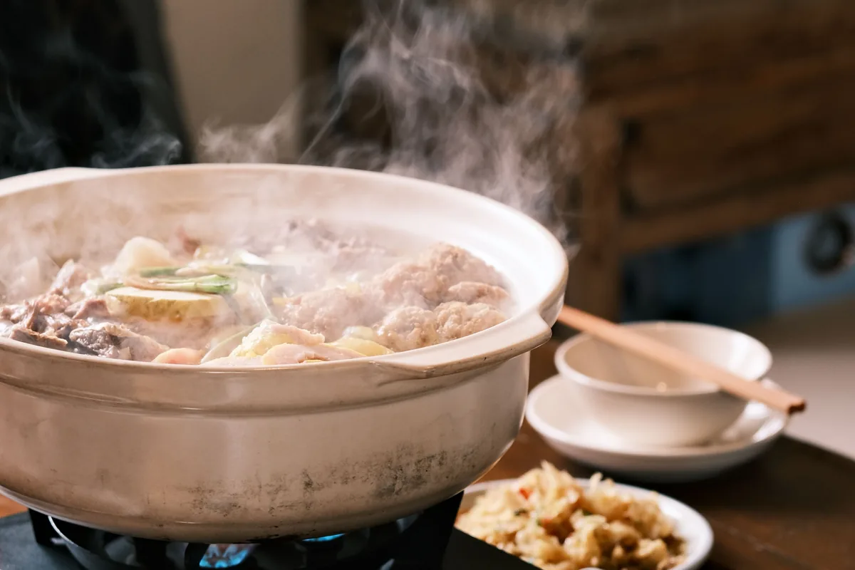 A steaming pot of chicken, tofu and vegetables in broth on a portable burner, representative of a chanko-style Japanese hot pot